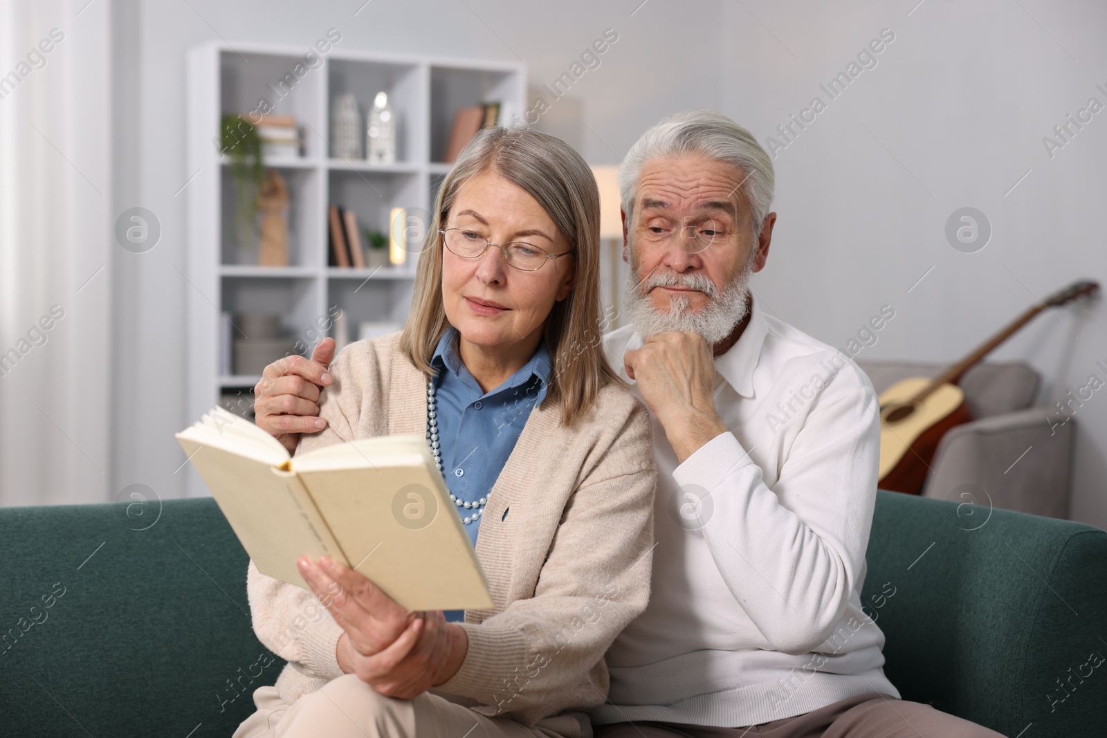 Photo of Cute elderly couple reading book together on sofa at home