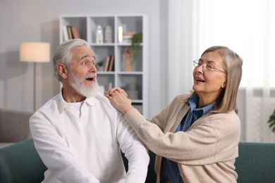 Cute elderly couple laughing on sofa at home