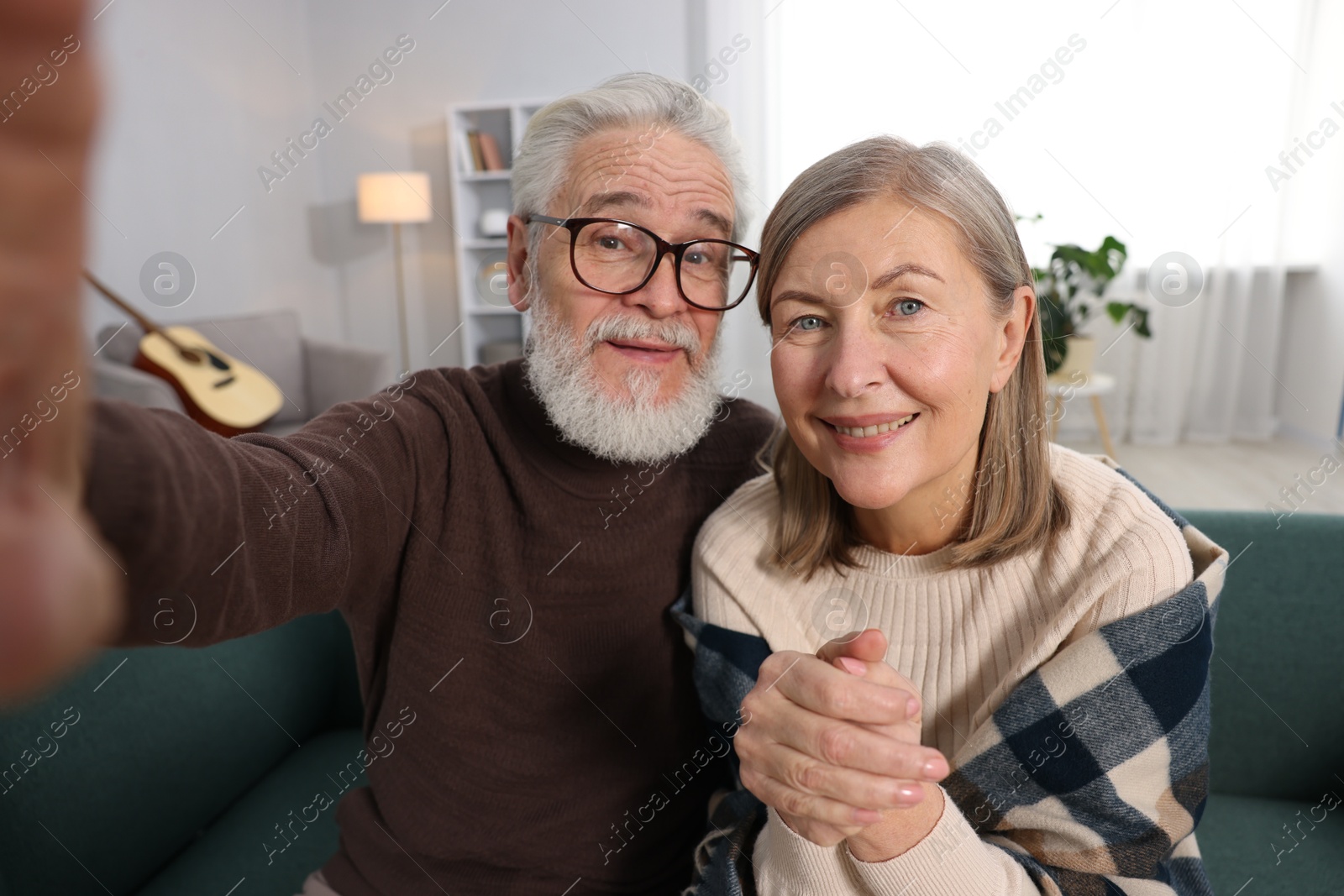 Photo of Happy elderly couple taking selfie on sofa at home