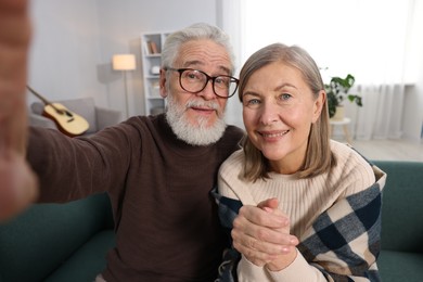 Happy elderly couple taking selfie on sofa at home