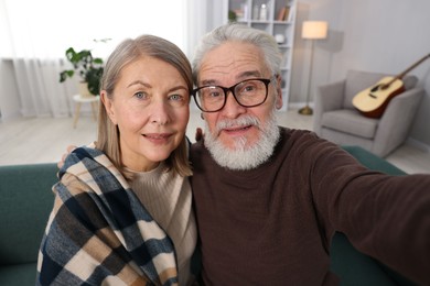 Photo of Happy elderly couple taking selfie on sofa at home