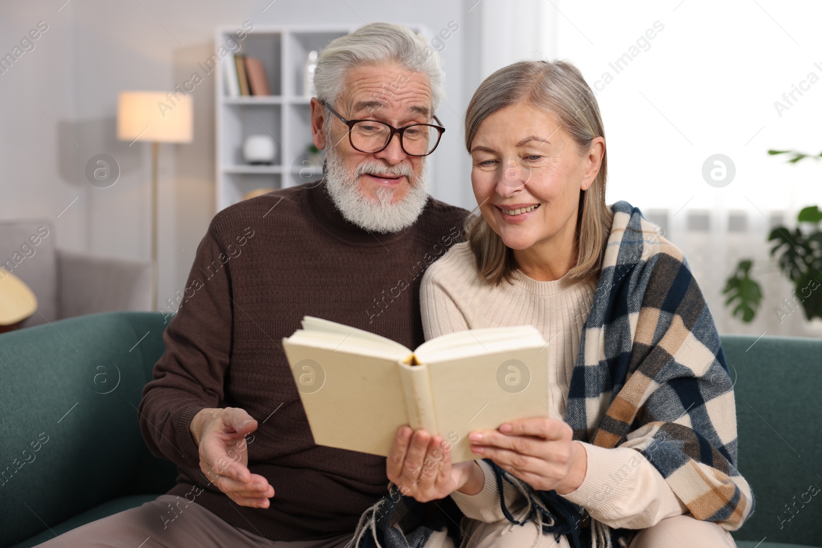 Photo of Happy elderly couple reading book together on sofa at home