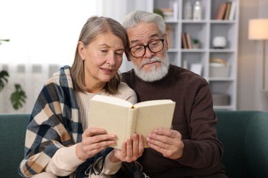 Cute elderly couple reading book together on sofa at home