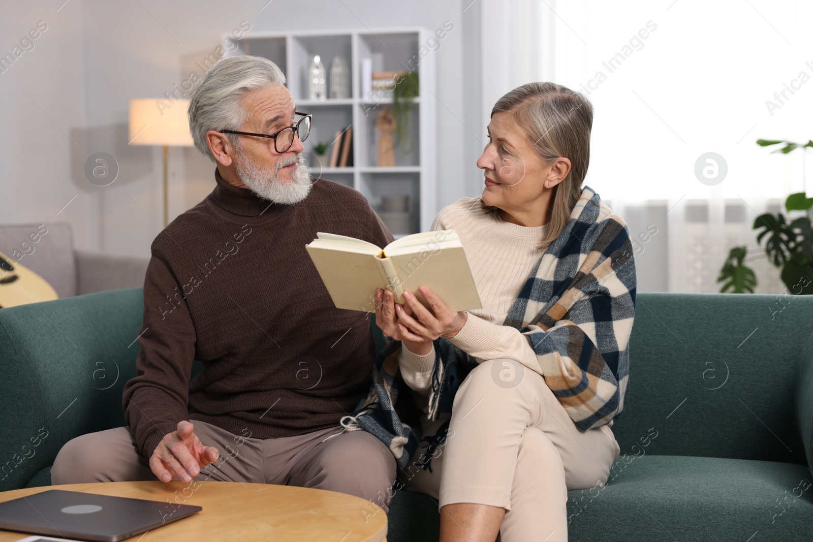 Photo of Cute elderly couple reading book together on sofa at home