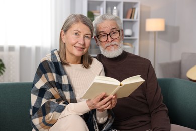 Cute elderly couple reading book together on sofa at home