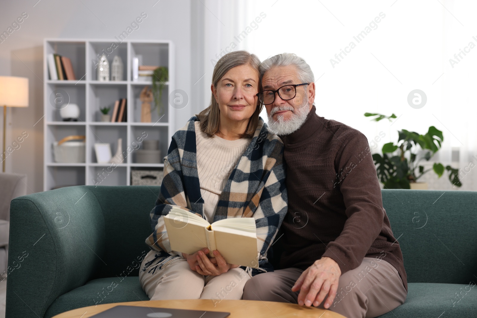 Photo of Cute elderly couple reading book together on sofa at home