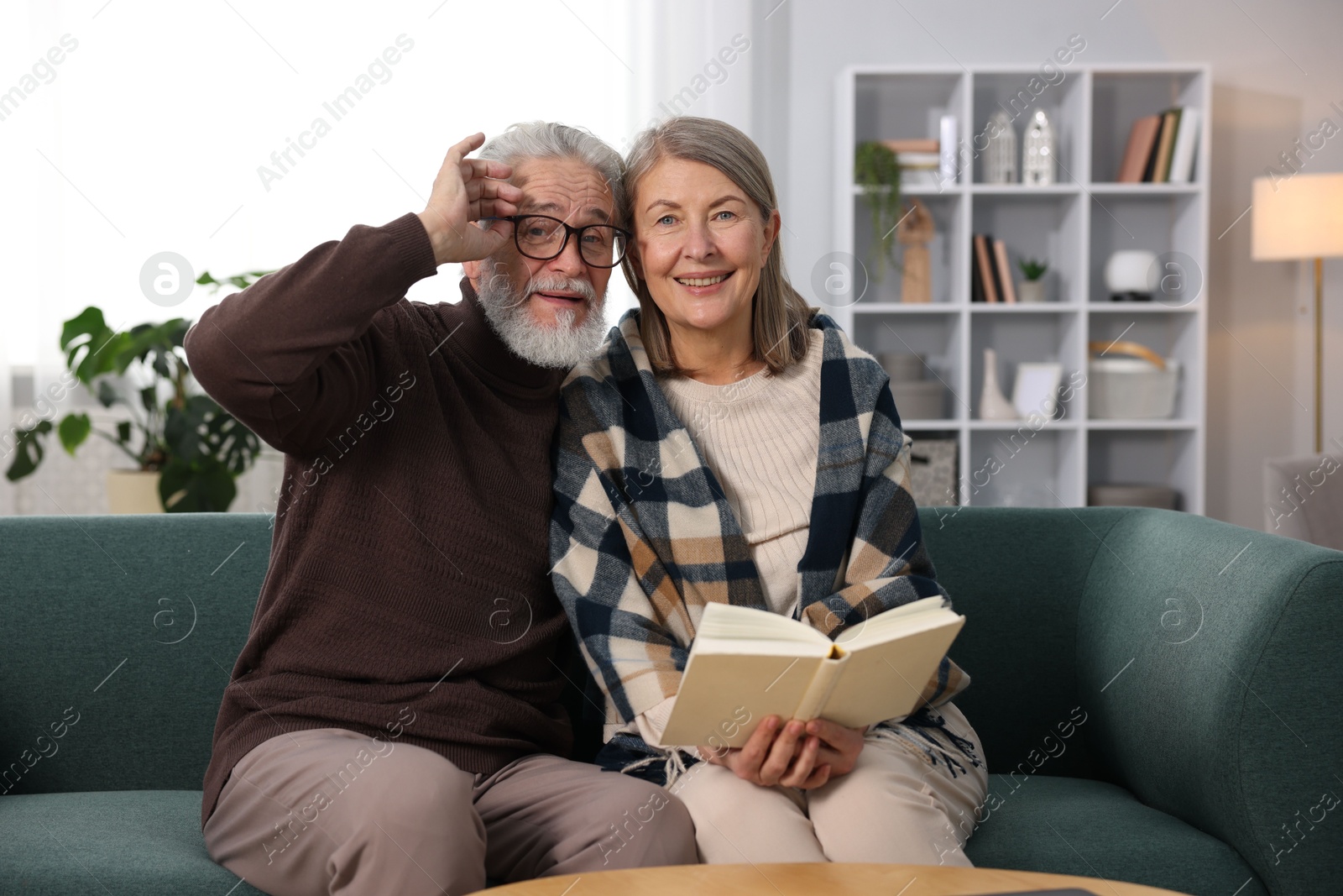 Photo of Happy elderly couple reading book together on sofa at home