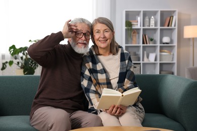 Happy elderly couple reading book together on sofa at home