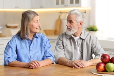 Photo of Cute elderly couple looking at each other at table in kitchen