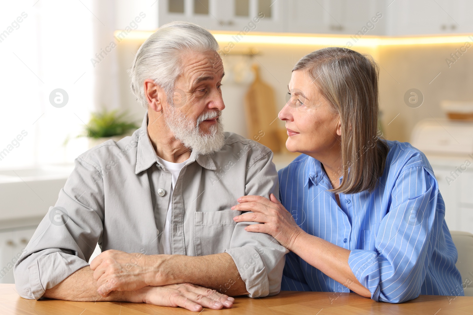 Photo of Cute elderly couple looking at each other at table in kitchen