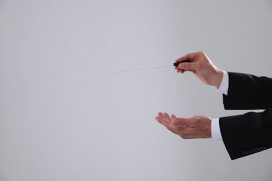 Professional conductor with baton on light grey background, closeup. Space for text