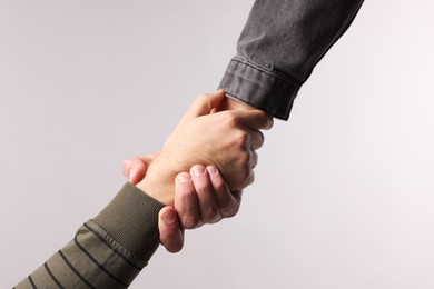 Photo of Help and support. People holding hands on light grey background, closeup