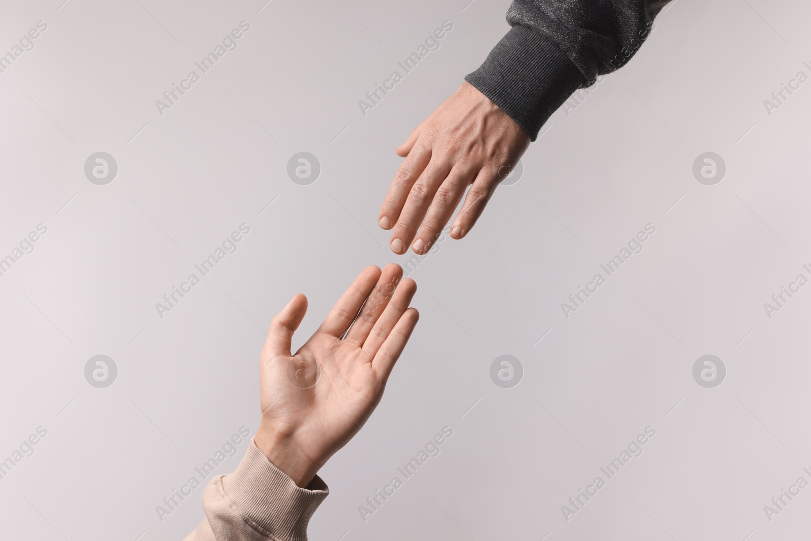 Photo of Man reaching for helping hand on light grey background, closeup