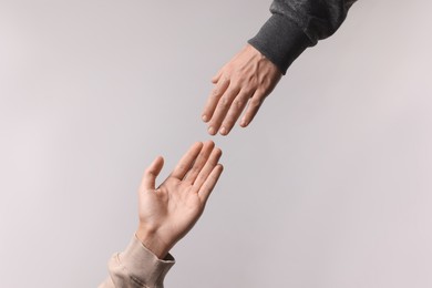 Man reaching for helping hand on light grey background, closeup