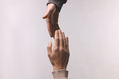 Man offering helping hand to his friend on light grey background, closeup