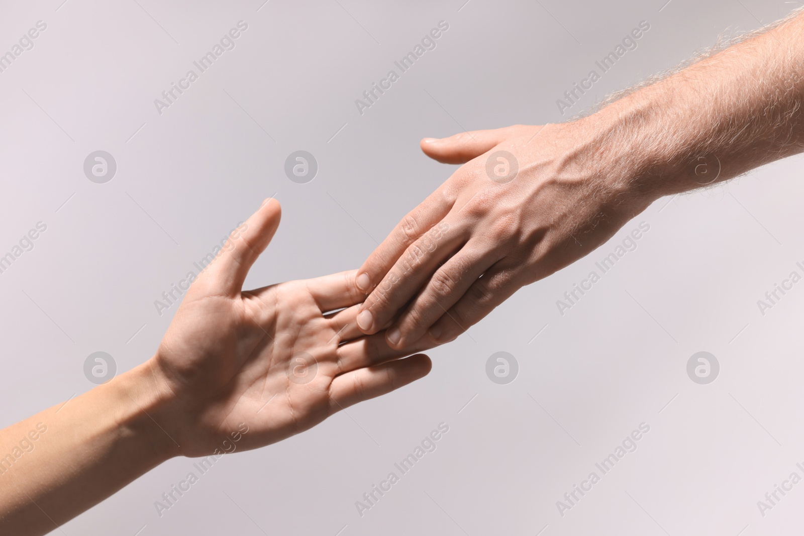 Photo of Man offering helping hand to his friend on light grey background, closeup