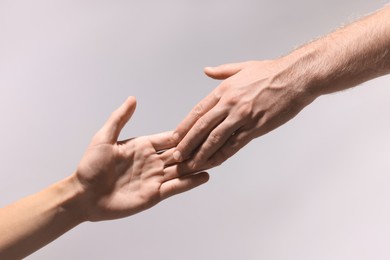 Man offering helping hand to his friend on light grey background, closeup