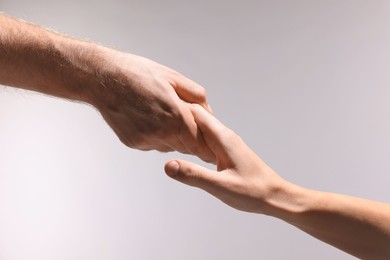 Photo of Help and support. People holding hands on light grey background, closeup