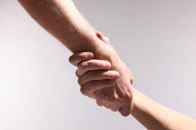 Photo of Help and support. People holding hands on light grey background, closeup