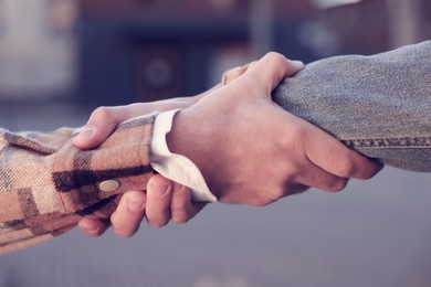 Help and support. People holding hands on city street, closeup