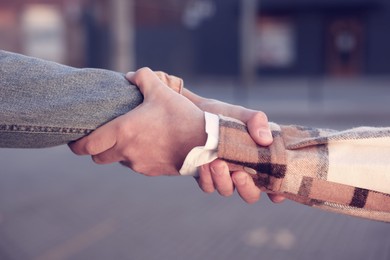 Help and support. People holding hands on city street, closeup