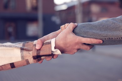 Help and support. People holding hands on city street, closeup