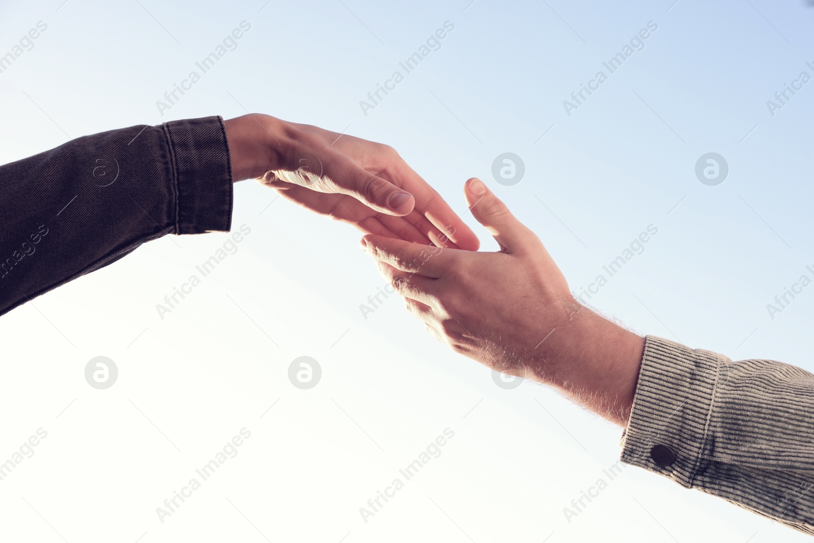 Photo of Man offering helping hand to his friend against blue sky, closeup