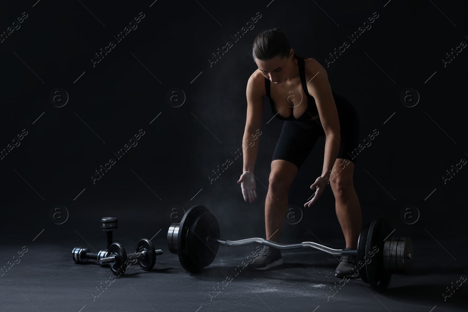 Photo of Woman with talcum powder on hands training with barbell against black background