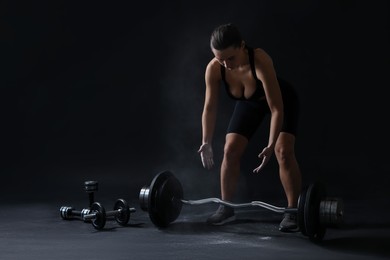 Photo of Woman with talcum powder on hands training with barbell against black background