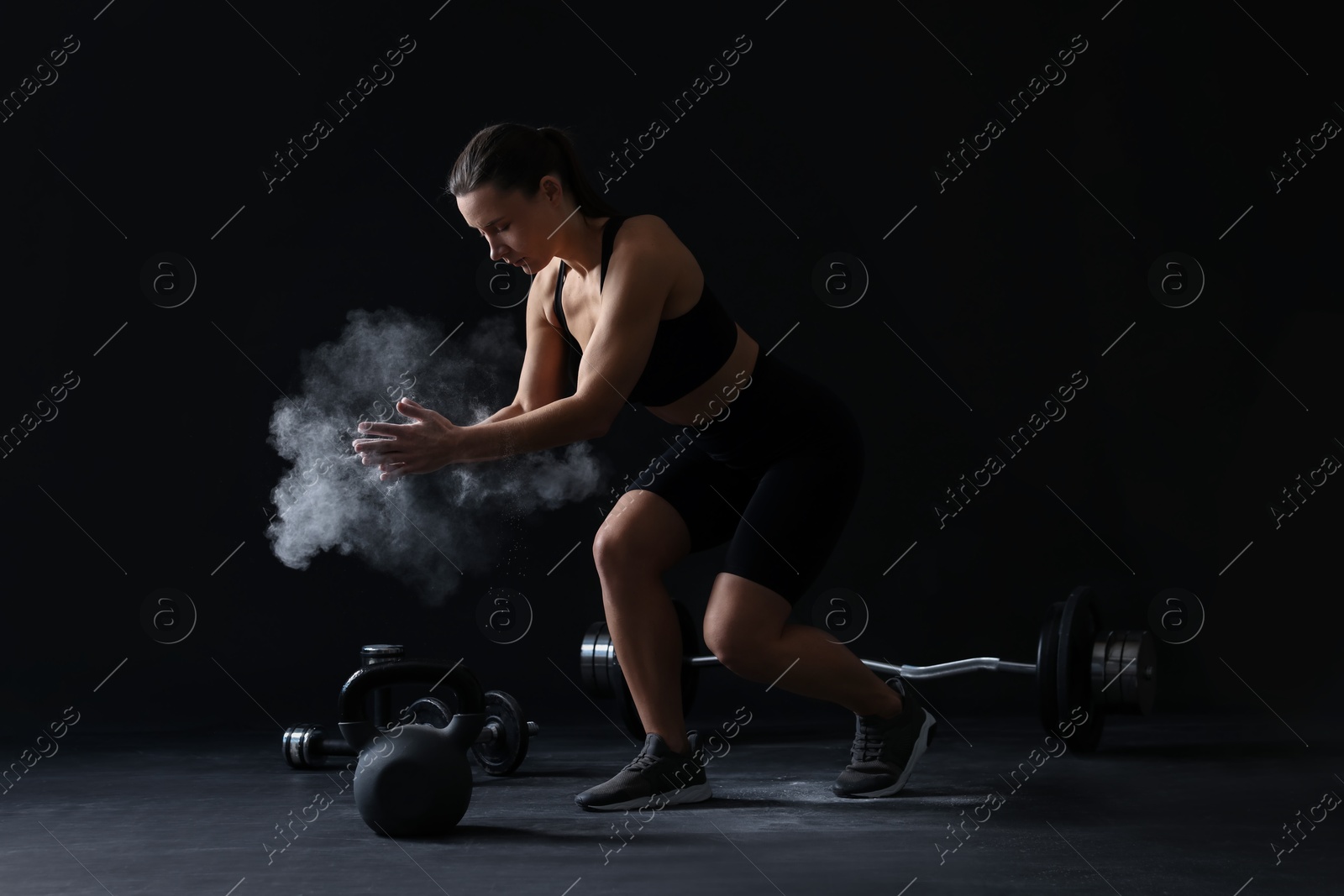 Photo of Woman clapping hands with talcum powder before training on black background