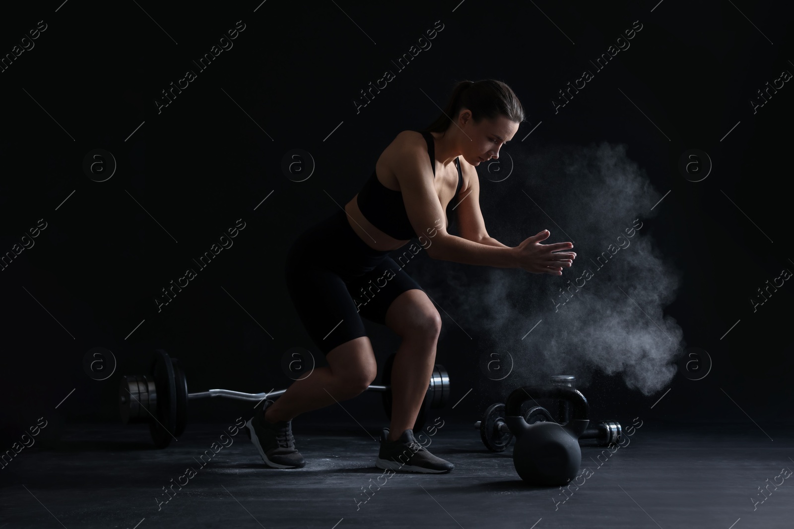 Photo of Woman clapping hands with talcum powder before training on black background