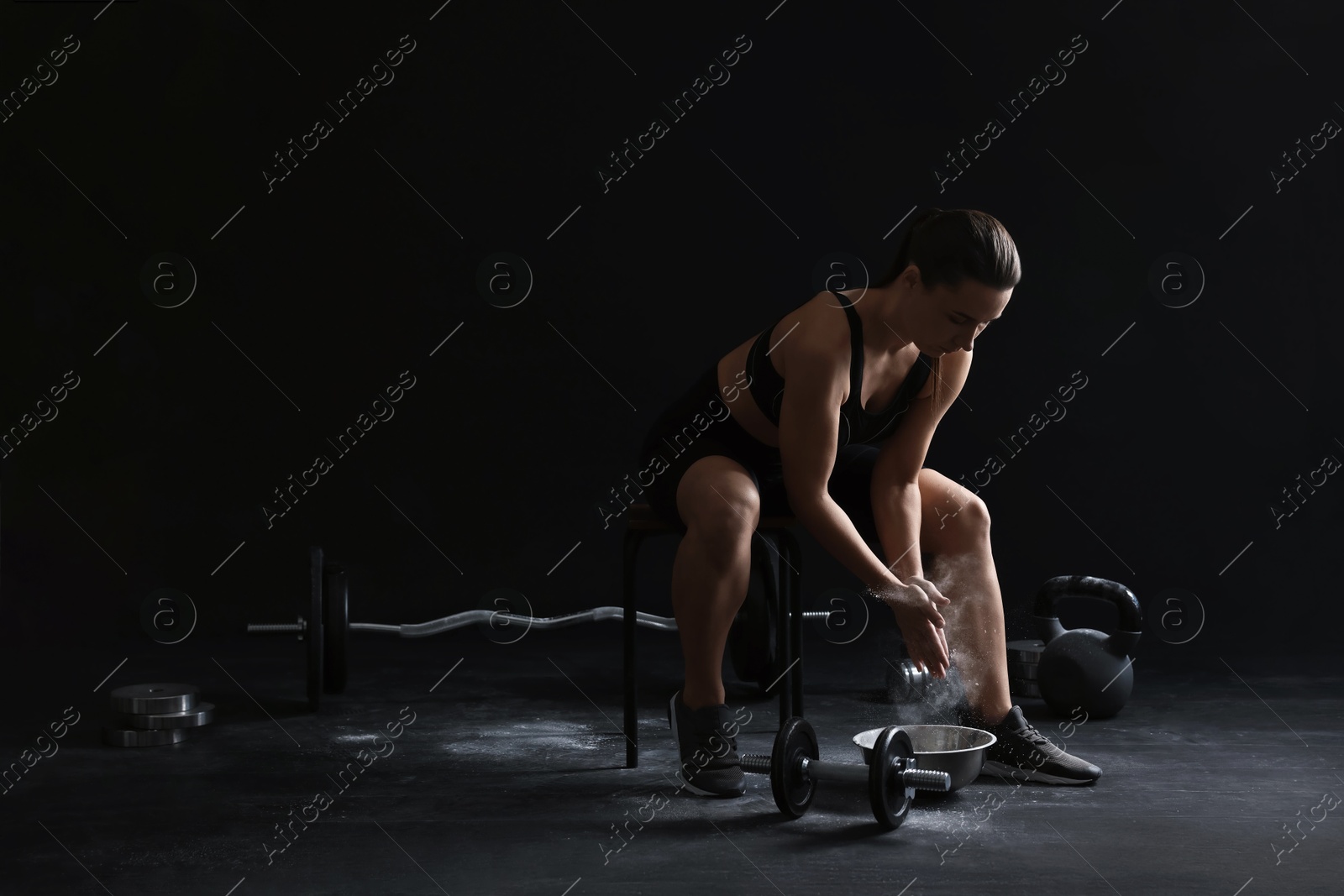 Photo of Woman applying talcum powder onto hands before training on black background