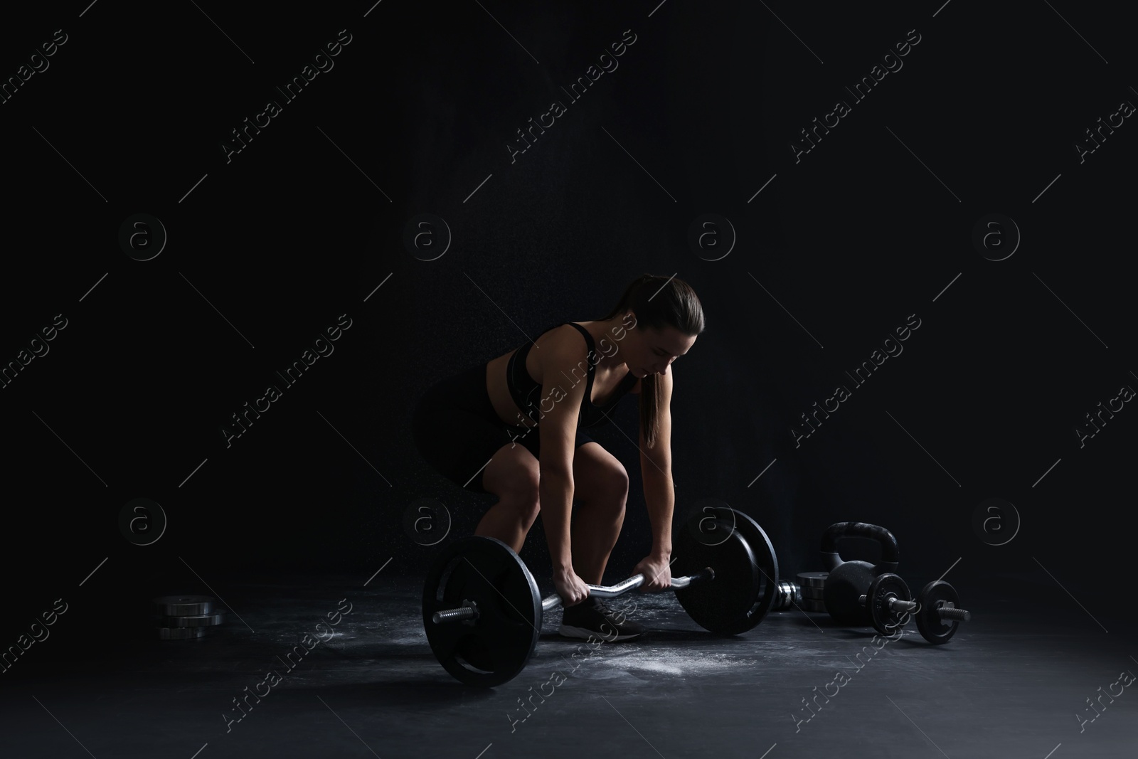 Photo of Woman training with barbell against black background