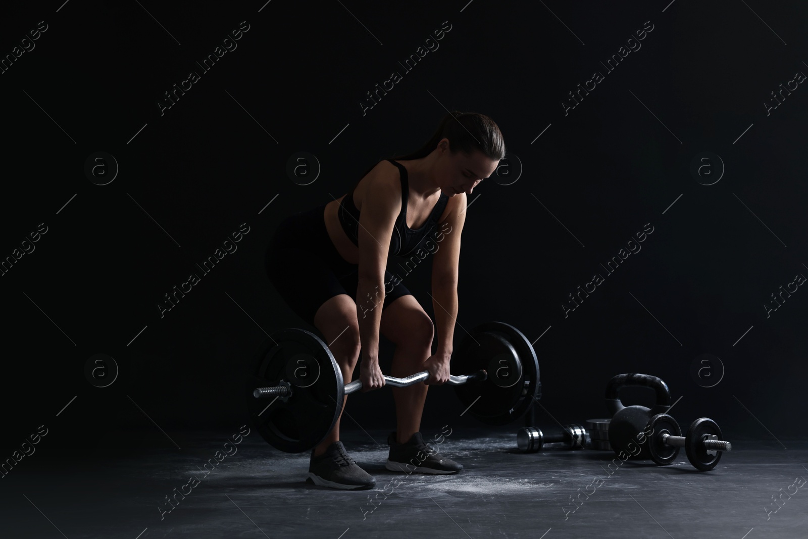 Photo of Woman training with barbell against black background