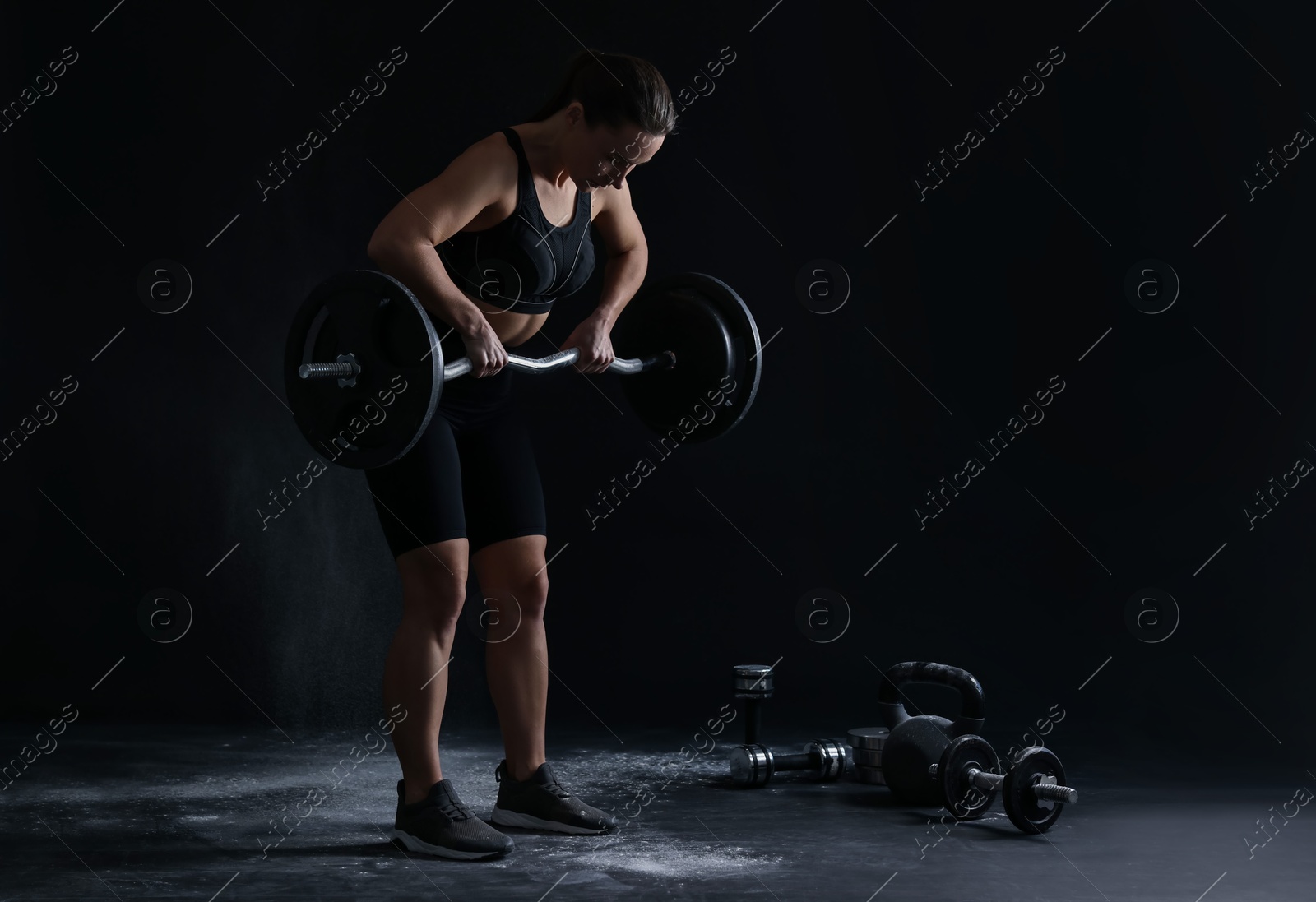 Photo of Woman training with barbell against black background