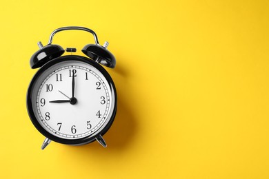 Photo of Black alarm clock on yellow background, top view. Space for text