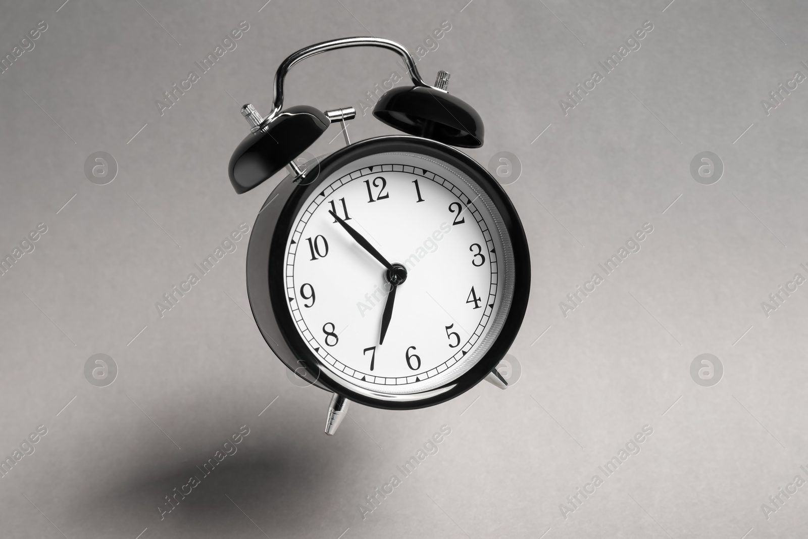 Black alarm clock in air on light grey background Photo of Black alarm clock in air on light grey background
