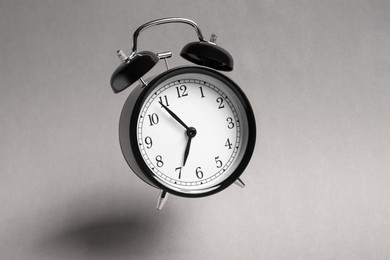 Photo of Black alarm clock in air on light grey background