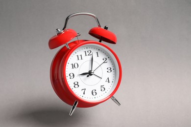 Photo of Red alarm clock in air on light grey background