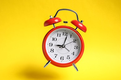 Photo of Red alarm clock in air on yellow background