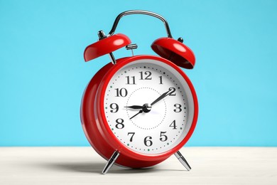 Photo of One red alarm clock on white wooden table against light blue background