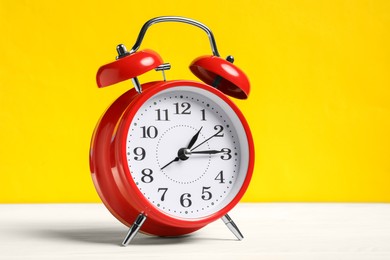 Photo of One red alarm clock on white wooden table against yellow background