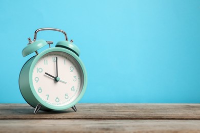 Photo of One turquoise alarm clock on wooden table against light blue background, space for text