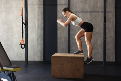 Photo of Sportswoman exercising on cube during crossfit workout in gym. Space for text