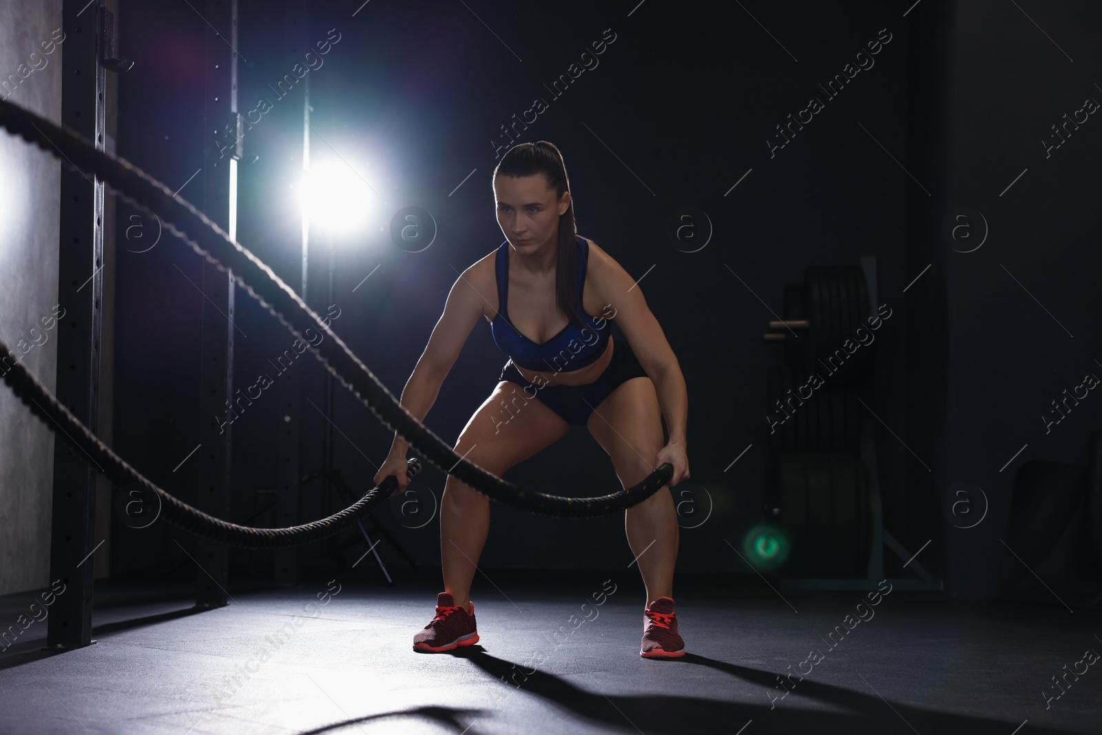 Photo of Sportswoman exercising with battle ropes during crossfit workout in gym