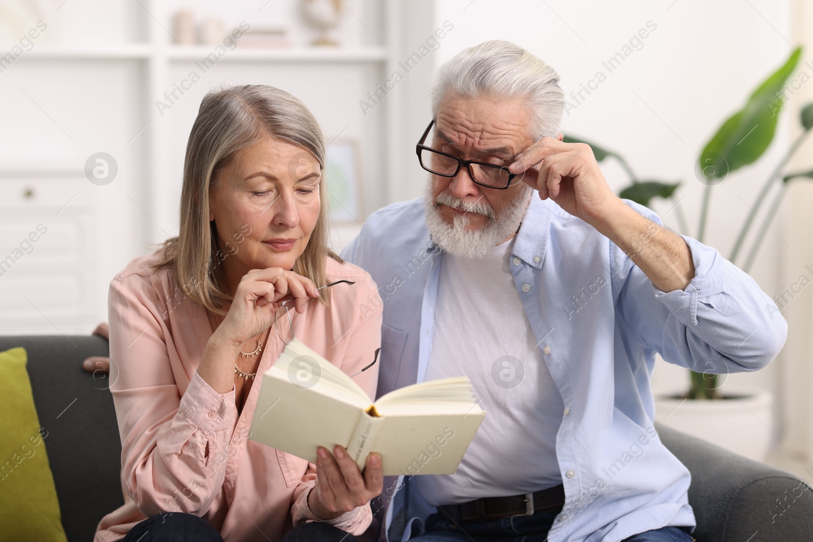 Photo of Cute elderly couple reading book together on sofa at home