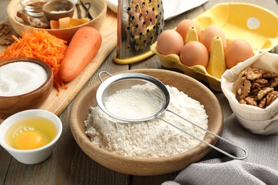 Photo of Different ingredients for making carrot cake and kitchenware on wooden table, closeup