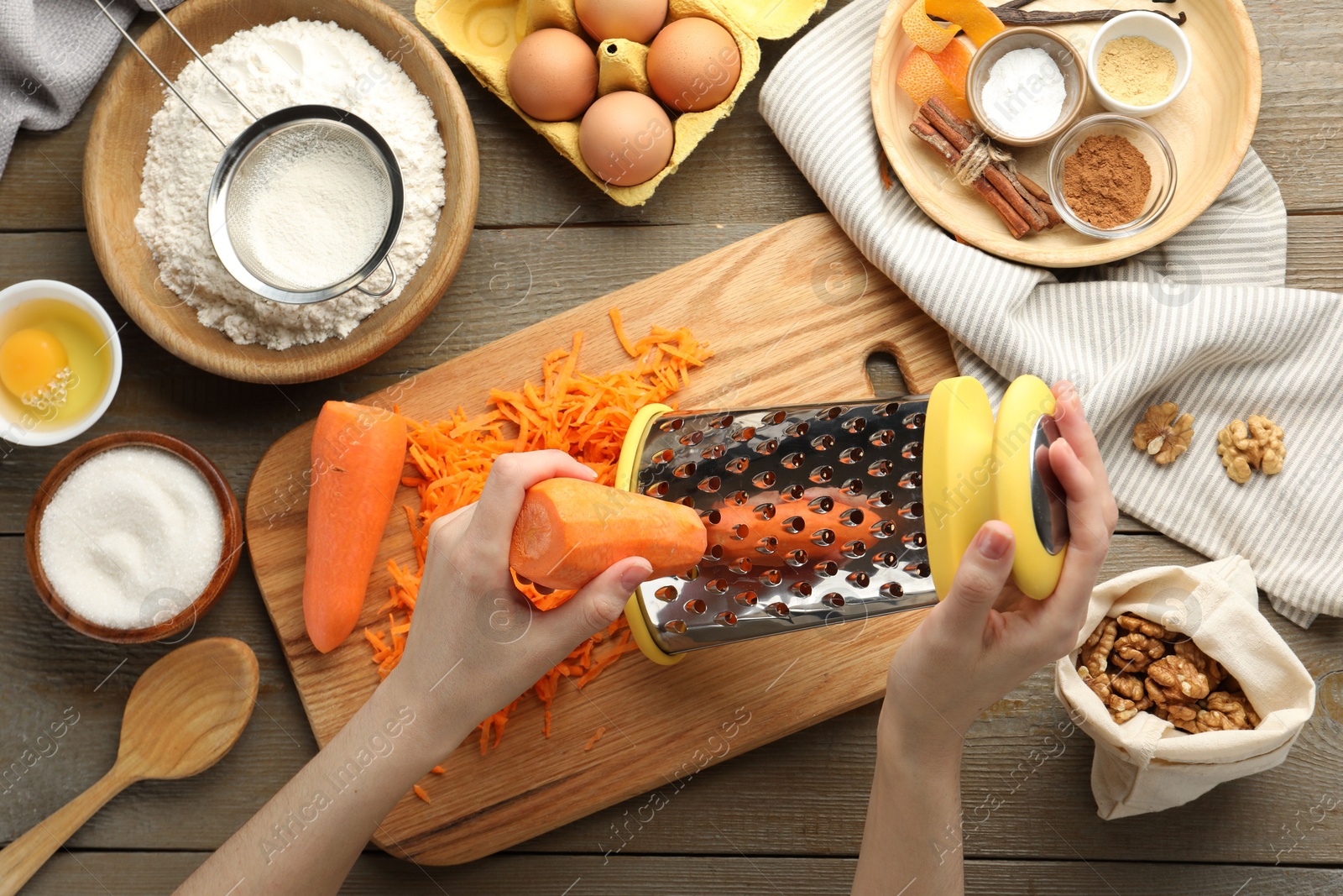 Photo of Making carrot cake. Woman grating vegetable at wooden table with ingredients, top view