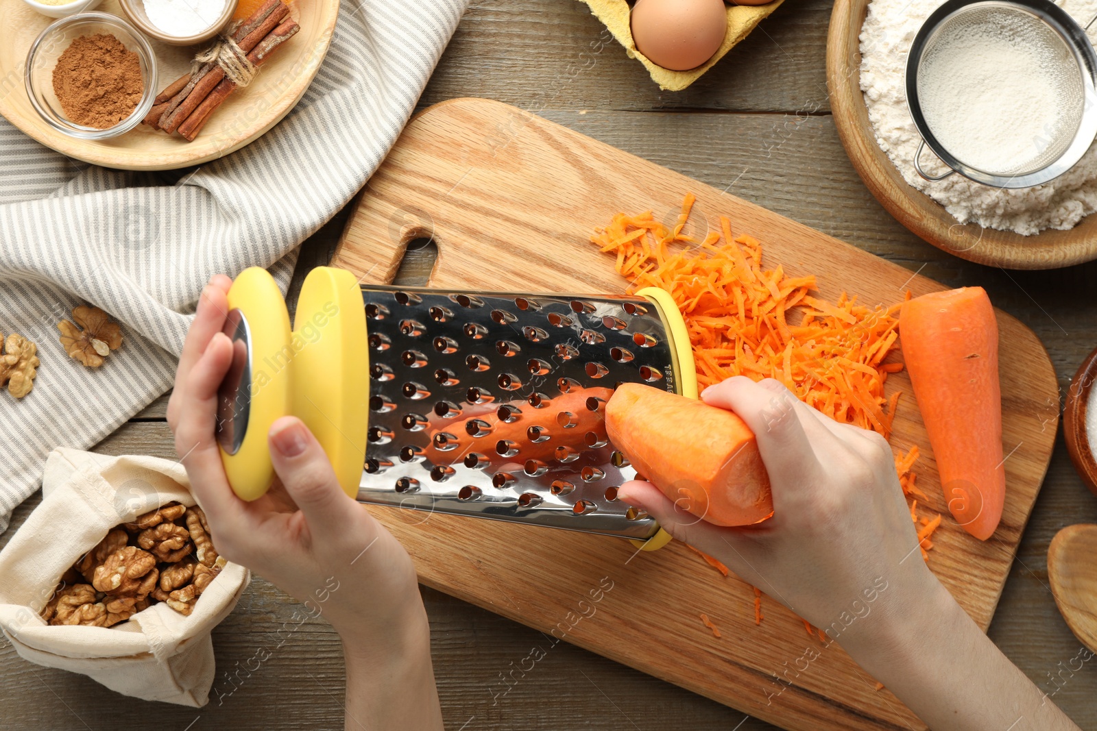 Photo of Making carrot cake. Woman grating vegetable at wooden table with ingredients, top view