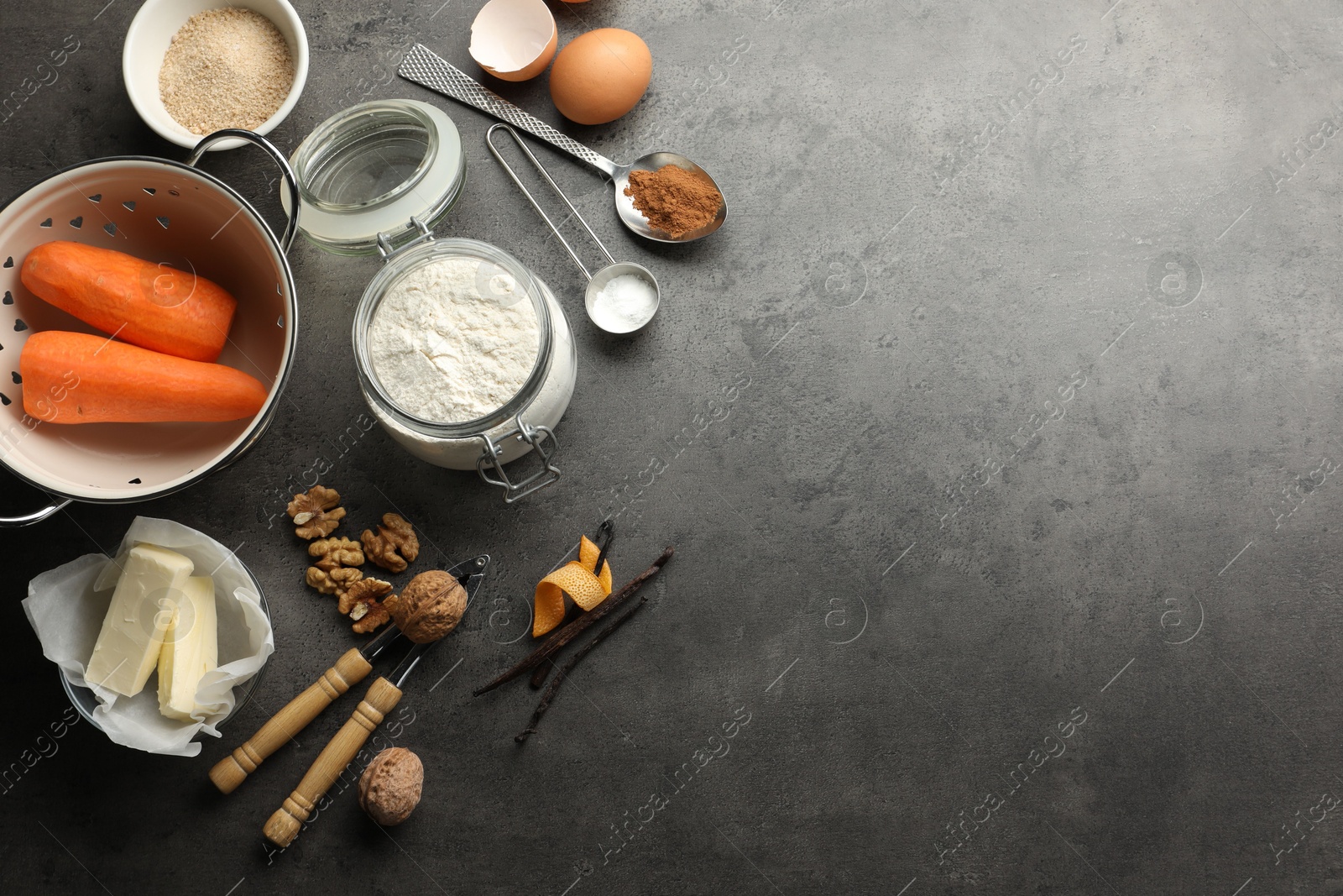 Photo of Different ingredients for making carrot cake and kitchenware on dark textured table, flat lay. Space for text